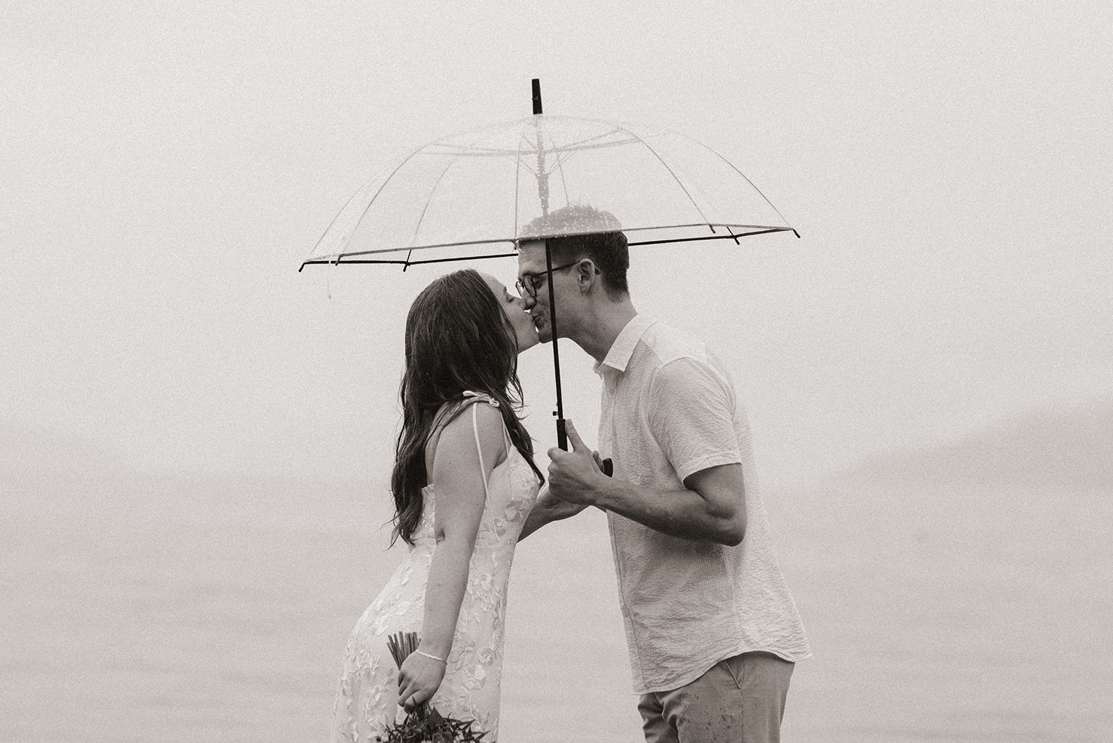 A black and white photo of a couple kissing under an umbrella